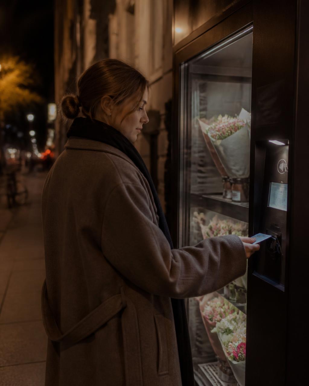 The same woman stopping at an elegant automatic flower machine on her way home, paying contactlessly